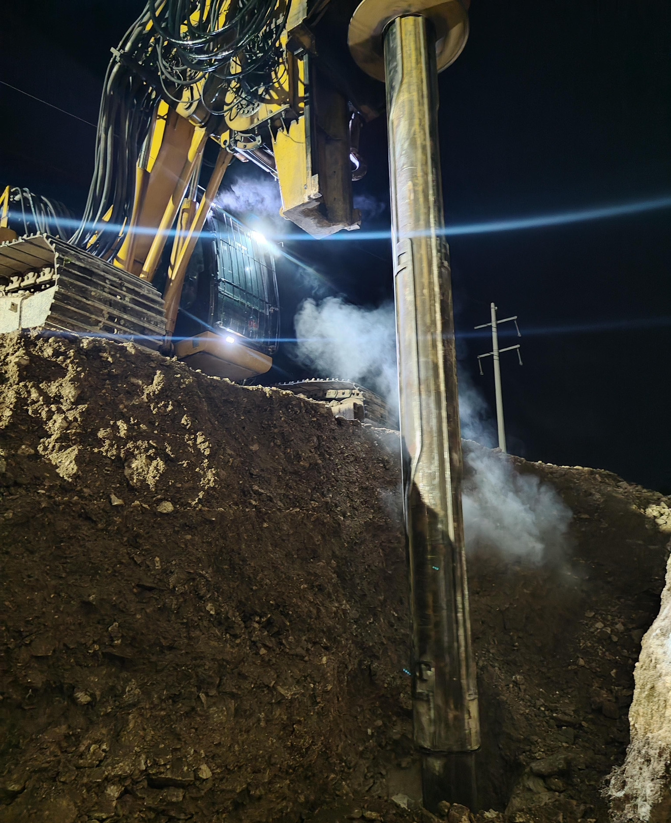 Perforadora trabajando de noche dentro de la excavación, con el ademe descendiendo al barreno